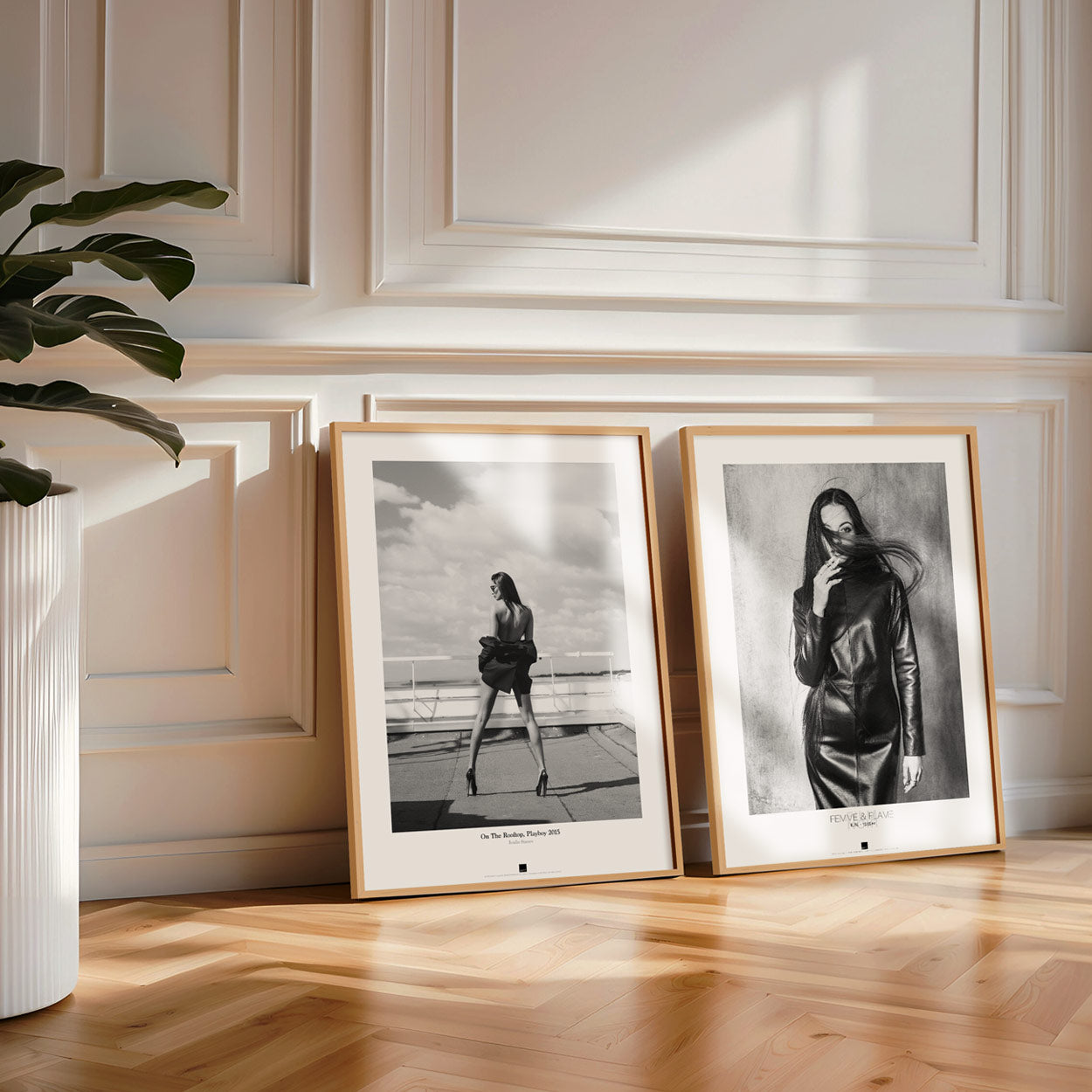 Two framed black-and-white portraits of women rest on a wood floor against a paneled wall, with sunlight casting shadows nearby.