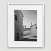 Narrow passageway between textured white walls, sunlight casting geometric shadows on the stone ground.