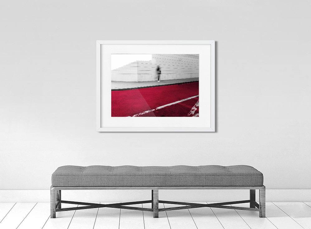A limited edition museum-quality photograph featuring an abstract urban scene with a predominantly red color, a white geometric pattern, and a small figure in the distance.