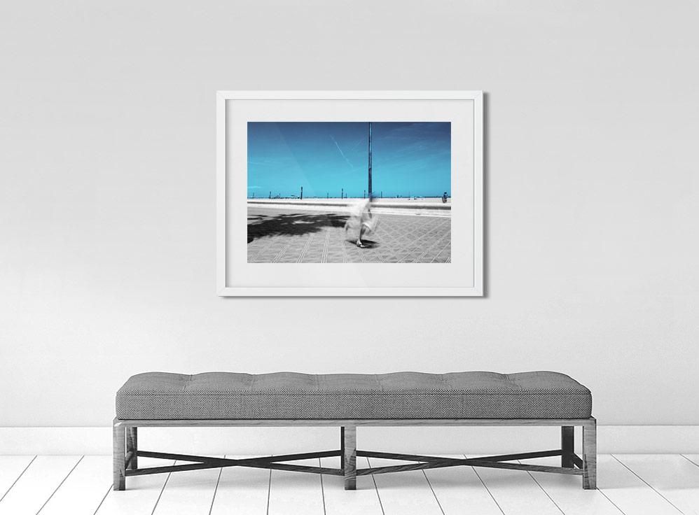 A limited edition gallery-quality photograph featuring a person in motion, possibly skateboarding, on a street with a clear blue sky in the background.