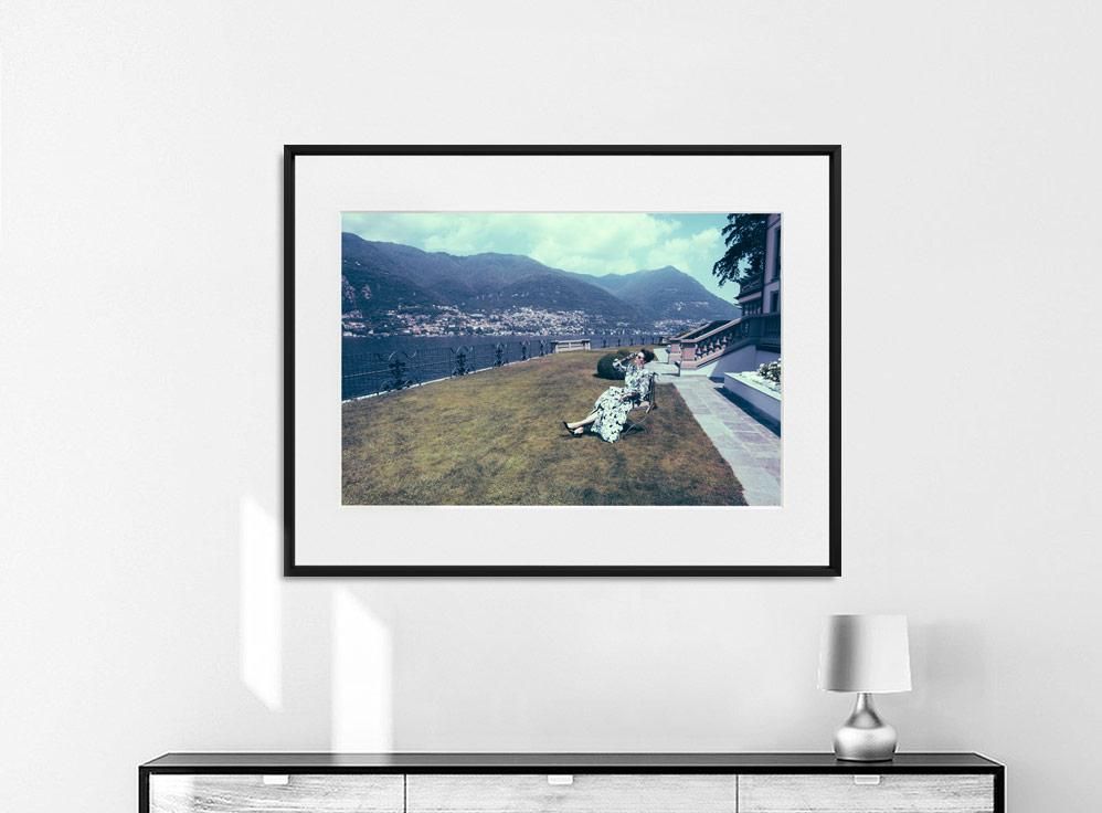 A framed color photograph shows a grassy slope beside a body of water, with distant mountains under a partly cloudy sky.