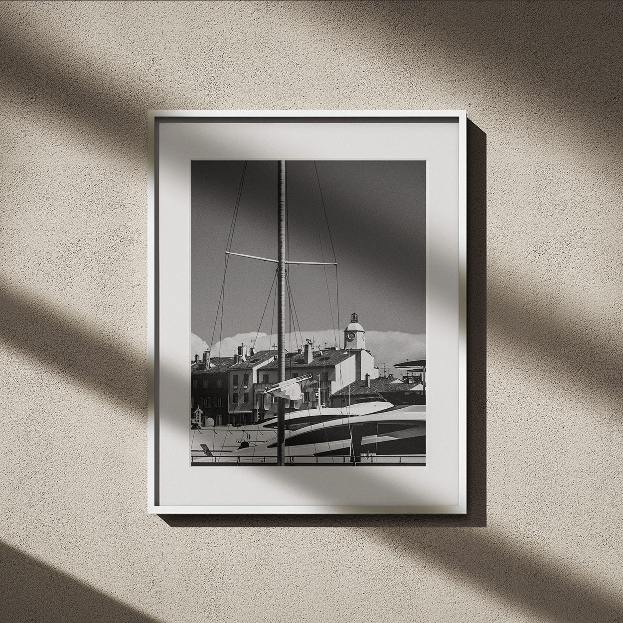 Framed black-and-white photograph showing a sailboat mast and rooftops with a clock tower in the background.