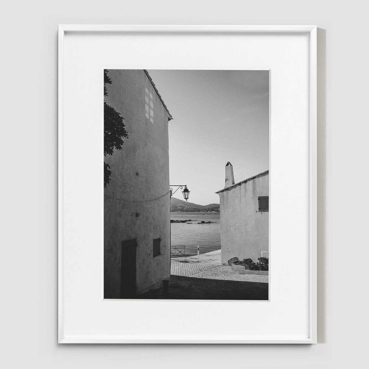 Narrow passageway between textured white walls, sunlight casting geometric shadows on the stone ground.