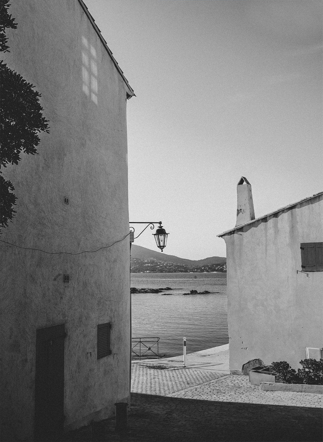 A narrow passageway with paved stones leads between whitewashed walls under bright sunlight.