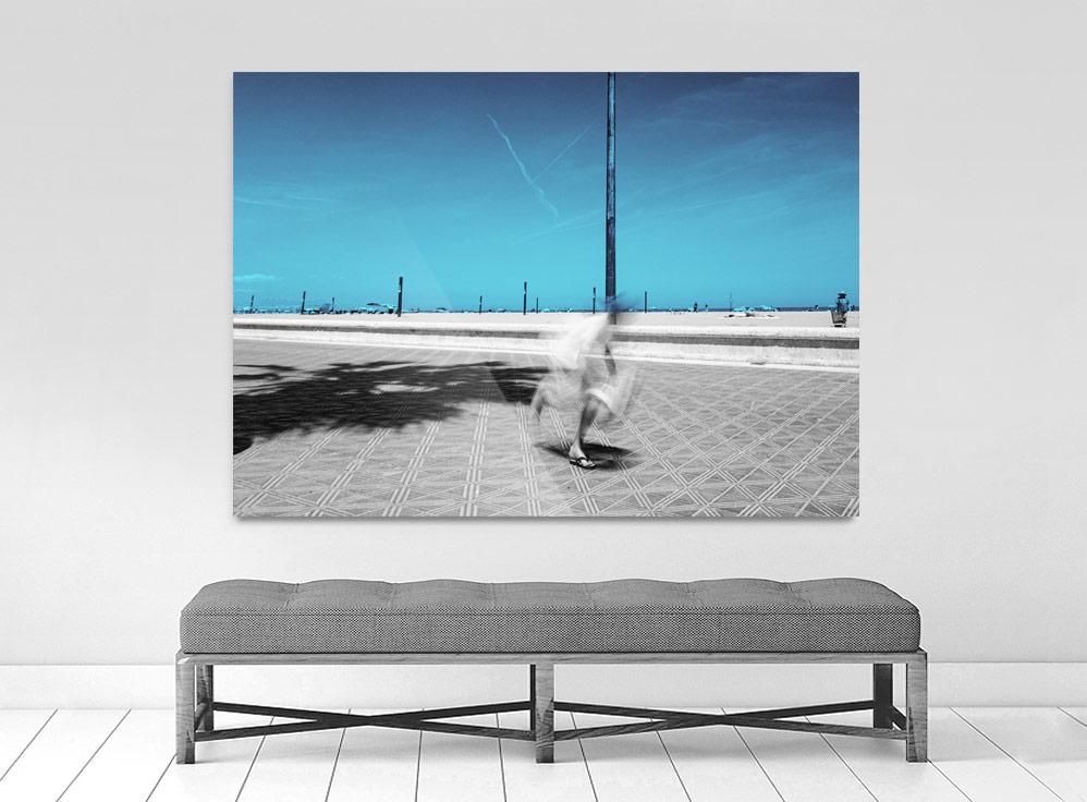 A limited edition gallery-quality photograph featuring a person in motion, possibly skateboarding, on a street with a clear blue sky in the background. The image has a white border and is presented in a black frame.