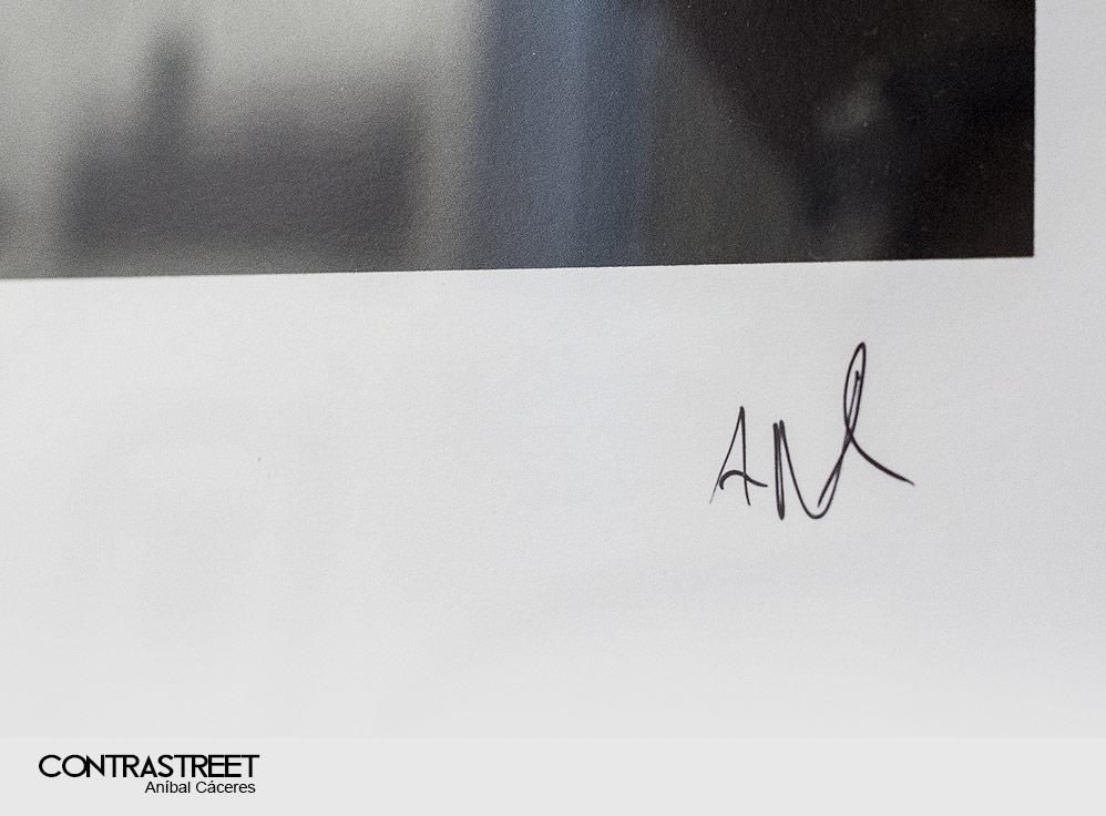 A handwritten signature in black ink appears on a white border below a blurred grayscale rectangular area.