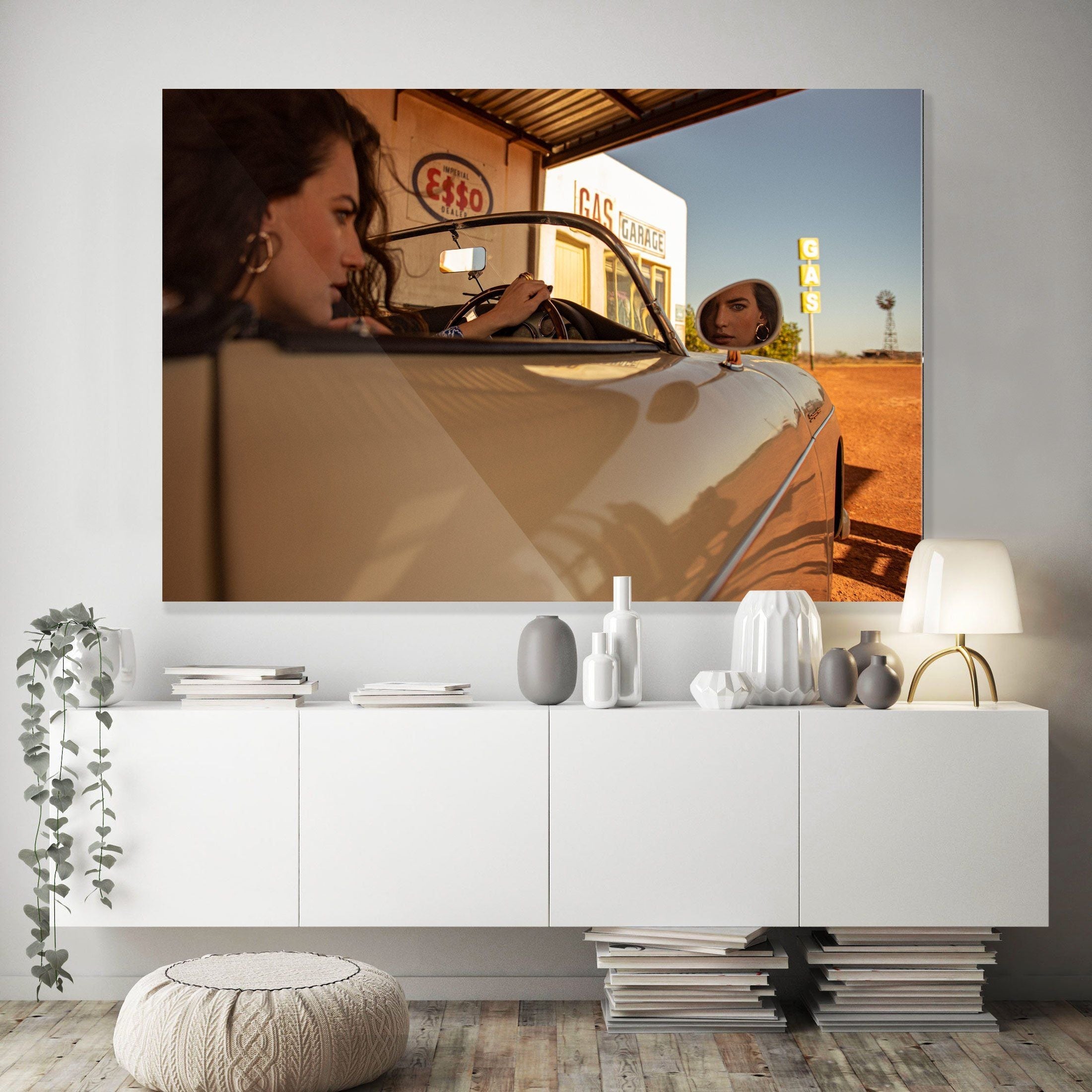 A large photograph above a white sideboard shows two women in a convertible at a gas station under clear blue sky.