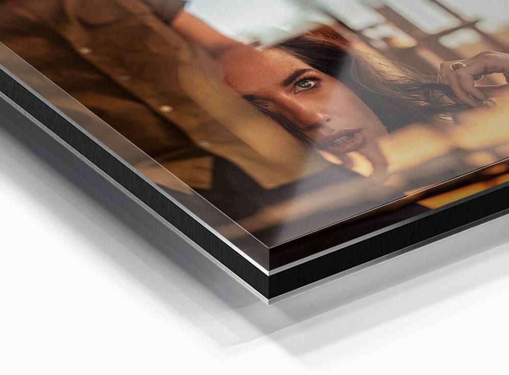 A close-up view of a glossy print featuring a partial portrait of a woman with dark hair, one eye visible, and warm indoor lighting.
