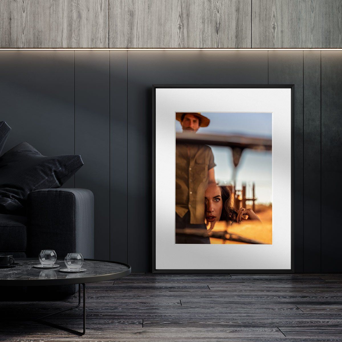 A large framed photograph rests against a dark wall, showing two people partially visible through a reflective surface.