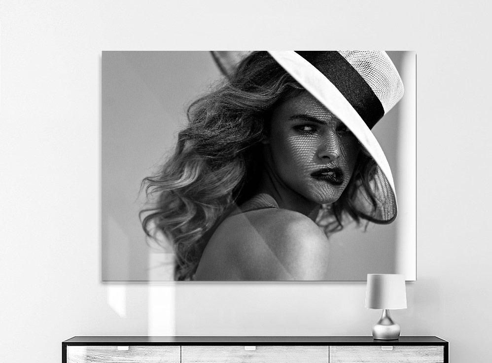 A woman with wavy hair wears a wide-brimmed hat at an angle, casting a mesh shadow across her face and shoulder.
