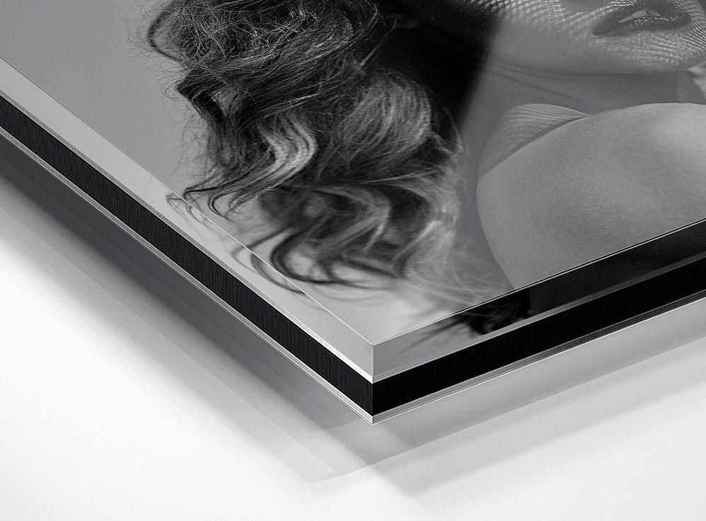 Section of a black and white portrait showing wavy hair, part of a face, and a shoulder, with a visible acrylic edge in the foreground.