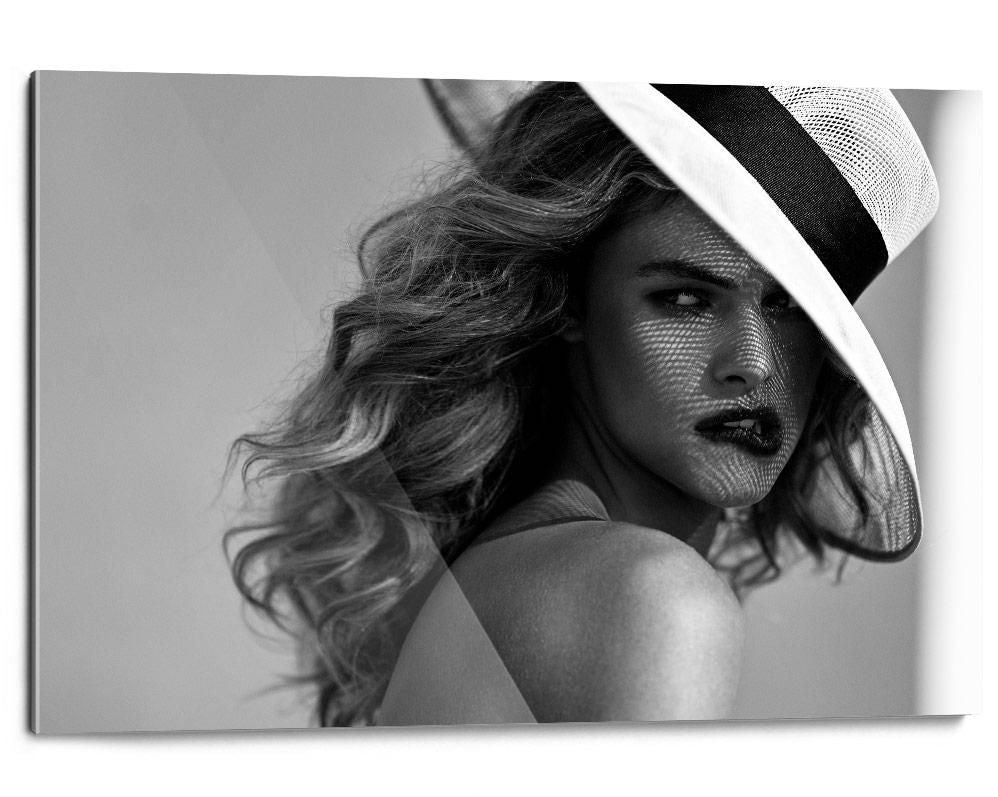 A person with wavy hair wears a wide-brimmed hat, with mesh shadows cast across their face in soft, even lighting.