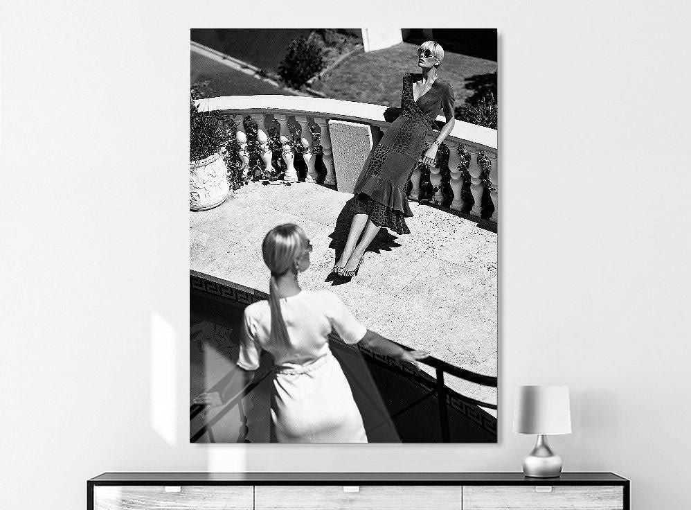 A large black-and-white photograph on a wall shows two women on a sunlit terrace, one leaning on a balustrade, the other seen from behind.