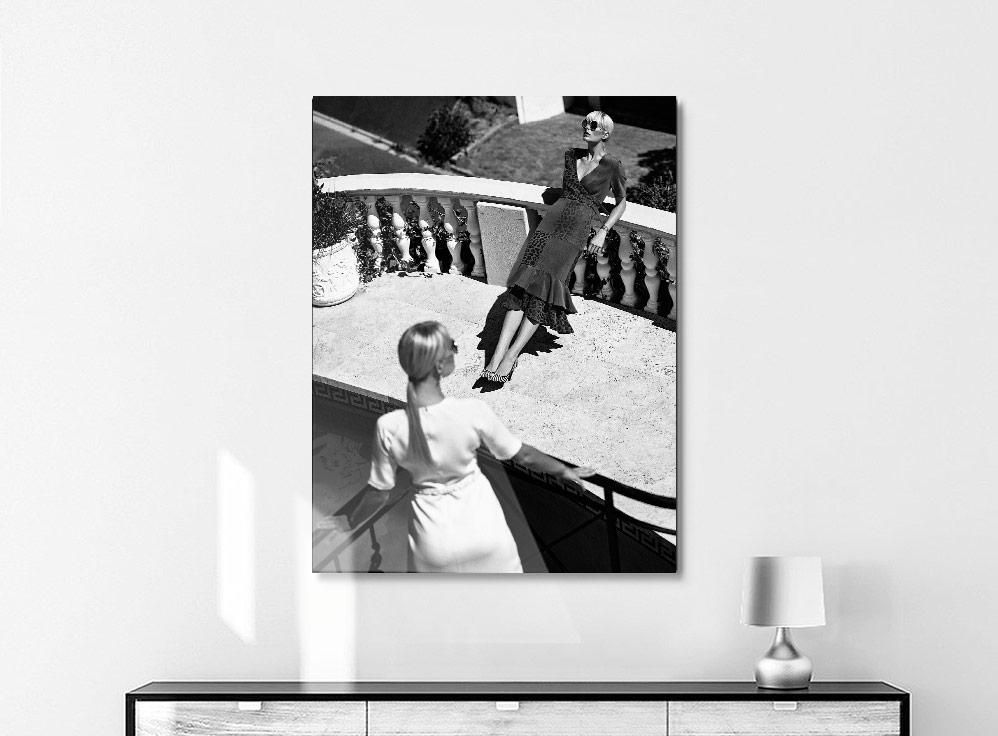 A framed black-and-white photograph shows two women on a sunlit terrace, one seated on a balustrade and another seen from behind.