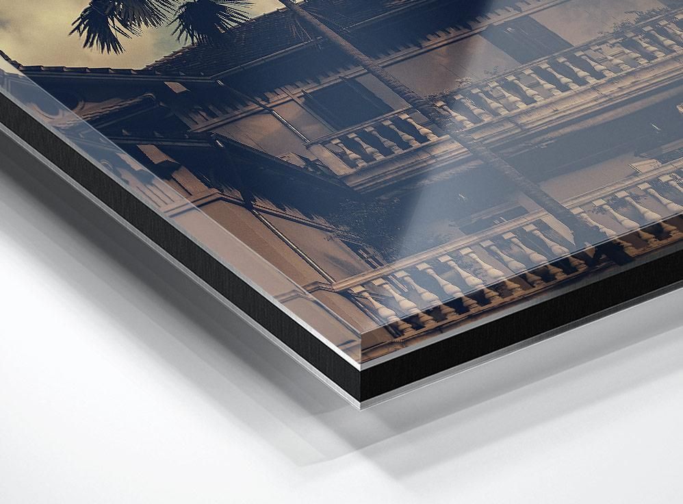 Corner detail of a layered print showing part of a building facade with balconies, palm fronds, and reflected light on the surface.