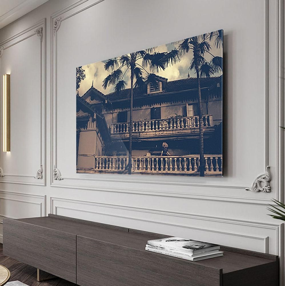 A framed photograph of a two-story building with balustrades and tall palm trees is mounted on a white paneled wall above a low cabinet.