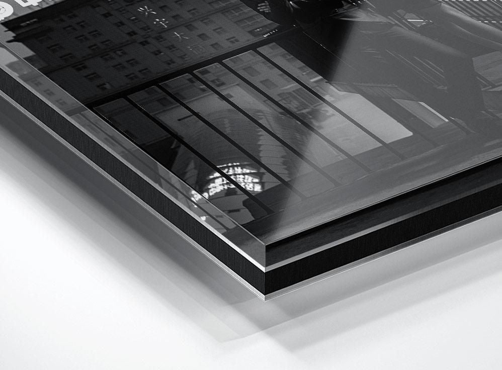A close view of a glossy print corner showing a black-and-white city scene with building facades and a metal railing in the foreground.